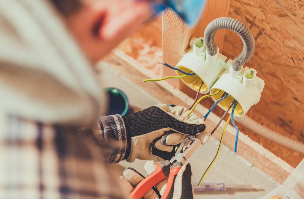 A worker uses tools to connect electrical wires at a construction site in the afternoon.
